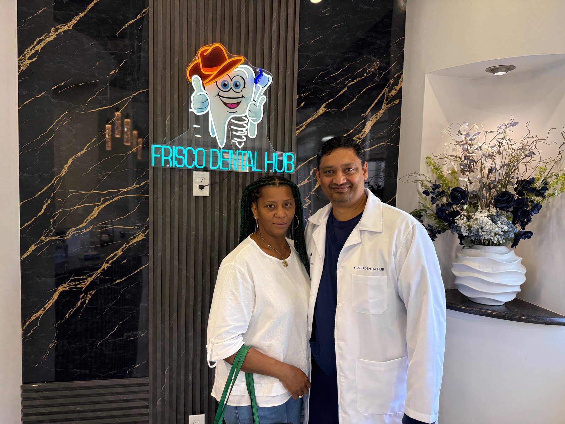 Dr. Chakrapani Nannapaneni, DDS, in his Frisco Dental Hub lab coat with a patient inside the practice's reception in Frisco, TX.